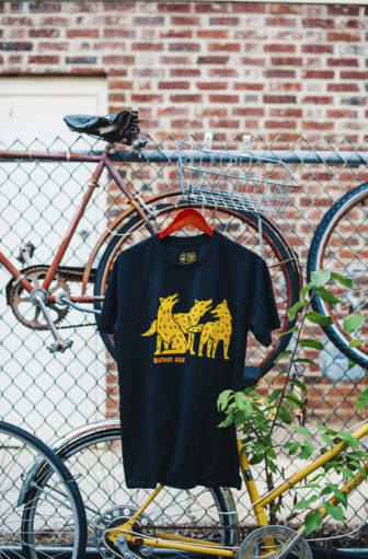 Bigfoot Kick wolf tshirt hanging onchainlink fence with bicycles in photo