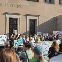 Alt text: A female protestor stands at a rally holding a home made sign that reads "Extinction is Forever"