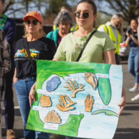 Alt text: A group of wildlife and climate activists stand on building steps holding colorful protest signs.