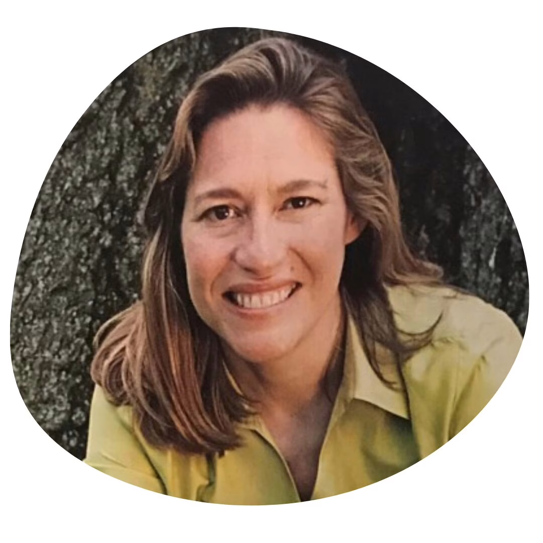 A person with long light brown hair, smiling and wearing a light green shirt, is pictured in front of a tree. The photo has an irregular rounded border.